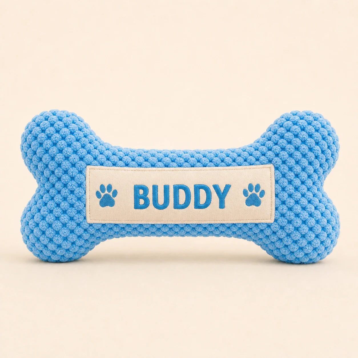 Personalized blue bone plush dog toy with Buddy name on warm studio background