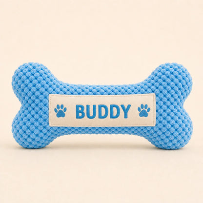 Personalized blue bone plush dog toy with Buddy name on warm studio background